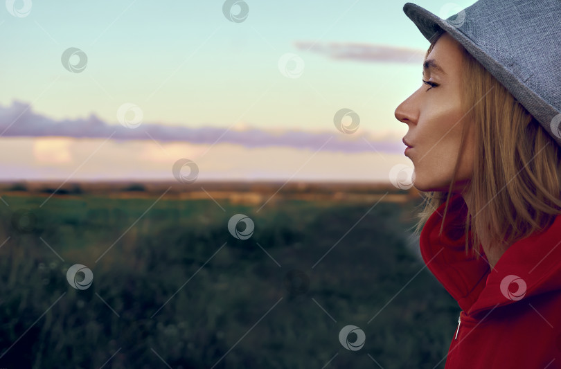 Скачать Девушка в красной куртке и шляпе посылает воздушный поцелуй. Молодая девушка на природе. сельская местность. Воздушный поцелуй. Фон фотосток Ozero