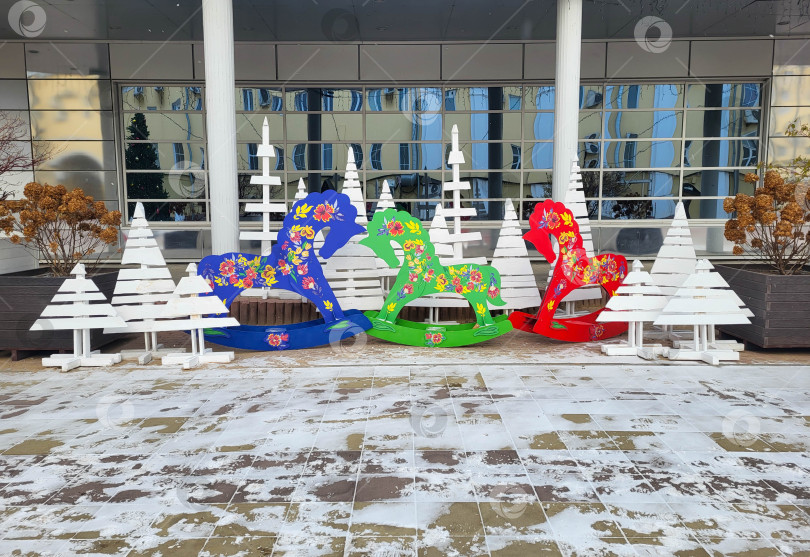 Скачать Россия, Ярославль, 11.12.2025 На улице для детей установлены деревянные белые рождественские елки и разноцветные лошадки-качалки. фотосток Ozero