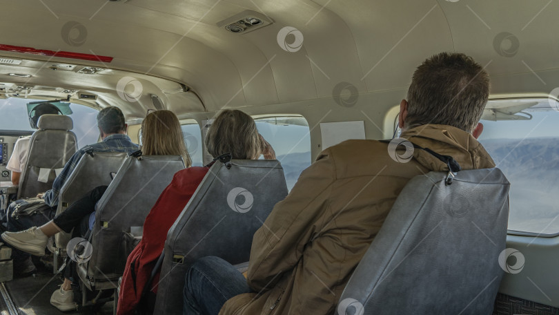Скачать Пассажиры сидят в ряд на сиденьях в небольшом самолете. фотосток Ozero