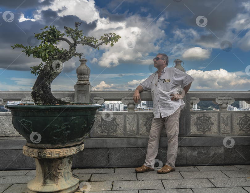 Скачать Мужчина стоит на террасе китайского храма, облокотившись на перила фотосток Ozero
