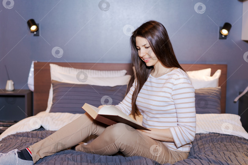 Скачать Женщина сидит на кровати и читает книгу фотосток Ozero