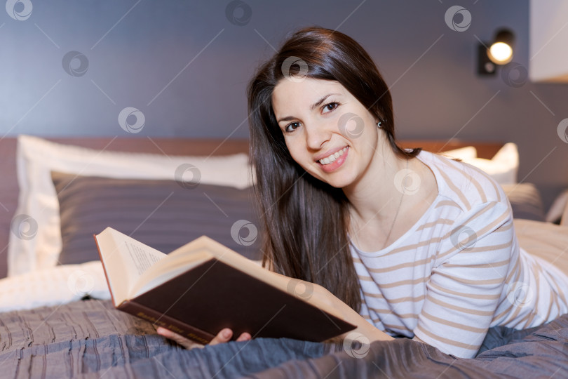 Скачать Женщина лежит на кровати с книгой в руке фотосток Ozero