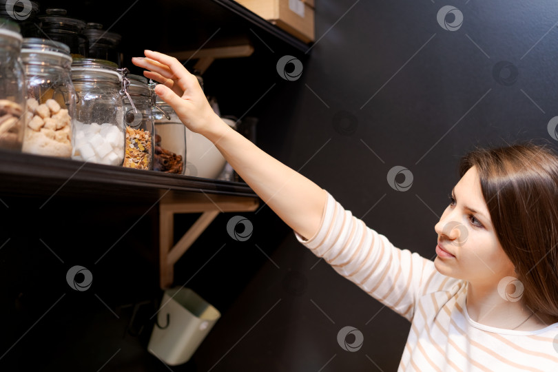 Скачать Женщина тянется к банке с орехами на полке фотосток Ozero