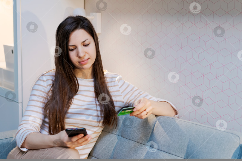 Скачать Женщина сидит на диване и смотрит в свой телефон фотосток Ozero