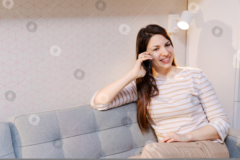 Скачать Женщина сидит на диване и разговаривает по мобильному телефону фотосток Ozero