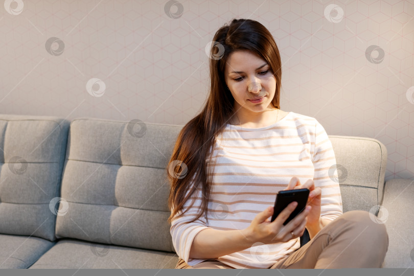Скачать Женщина сидит на диване и смотрит в свой мобильный телефон фотосток Ozero