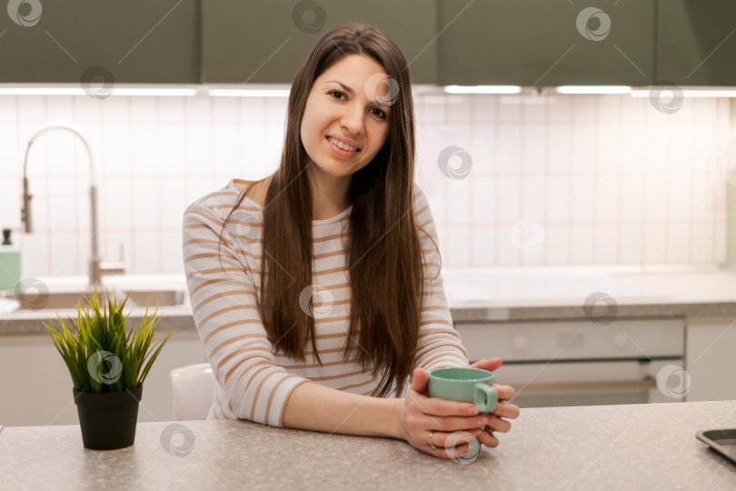 Скачать Женщина сидит за кухонным столом с кружкой в руке фотосток Ozero