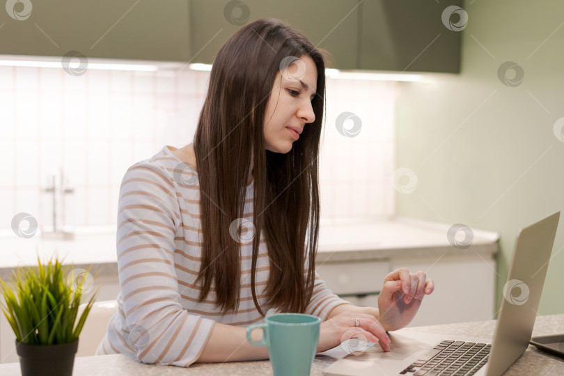 Скачать Женщина сидит за кухонным столом с ноутбуком и чашкой кофе фотосток Ozero