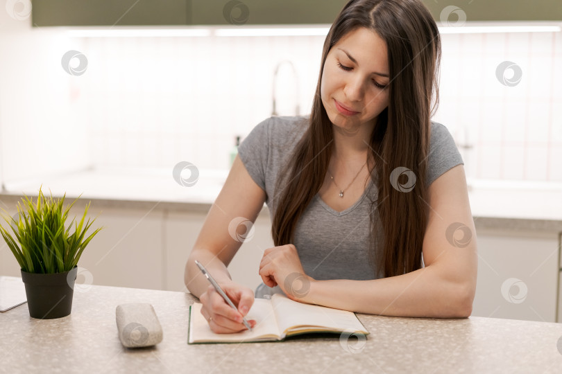 Скачать Женщина что-то пишет в блокноте, лежащем на кухонном столе фотосток Ozero