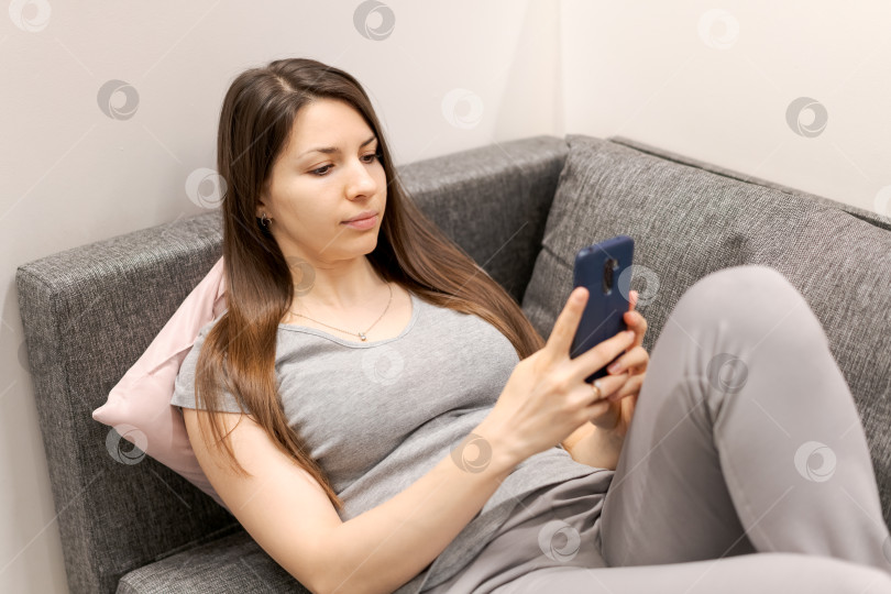 Скачать Женщина сидит на диване и смотрит в свой мобильный телефон фотосток Ozero