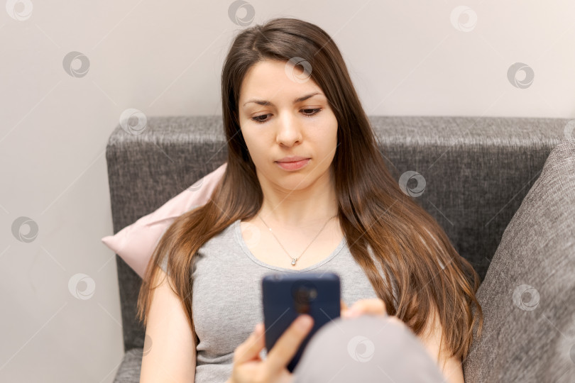 Скачать Женщина сидит на диване и смотрит в свой мобильный телефон фотосток Ozero