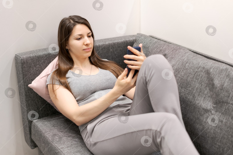 Скачать Женщина сидит на диване и смотрит в свой мобильный телефон фотосток Ozero