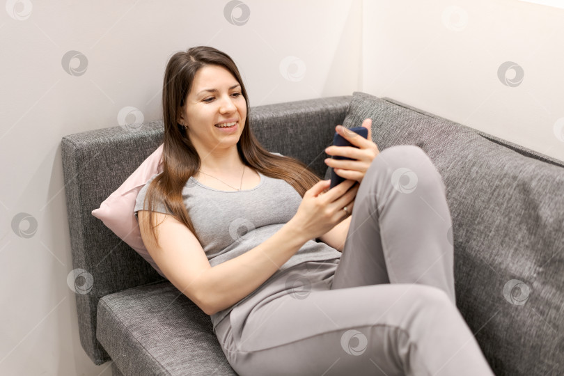 Скачать Женщина сидит на диване и смотрит в свой мобильный телефон фотосток Ozero