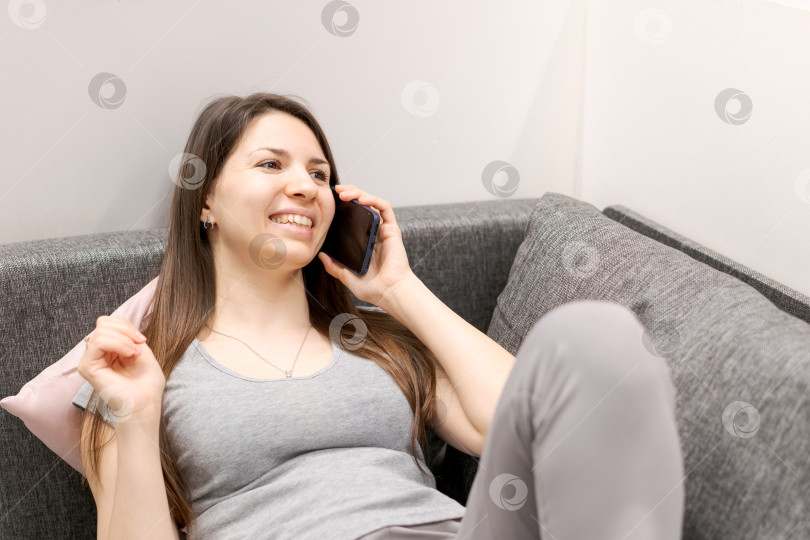 Скачать Женщина сидит на диване и разговаривает по мобильному телефону фотосток Ozero