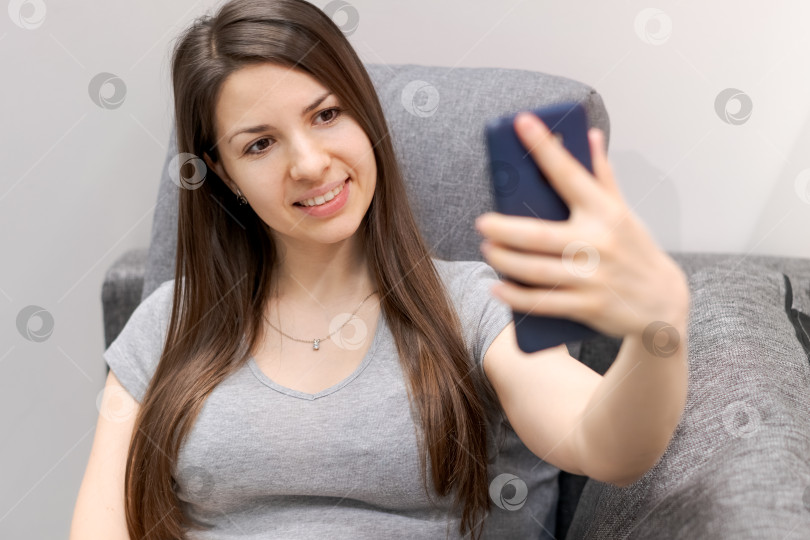 Скачать Женщина сидит на диване и делает селфи на свой мобильный телефон фотосток Ozero
