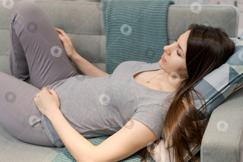 Скачать Женщина лежит на диване, скрестив ноги и подложив под голову подушку фотосток Ozero