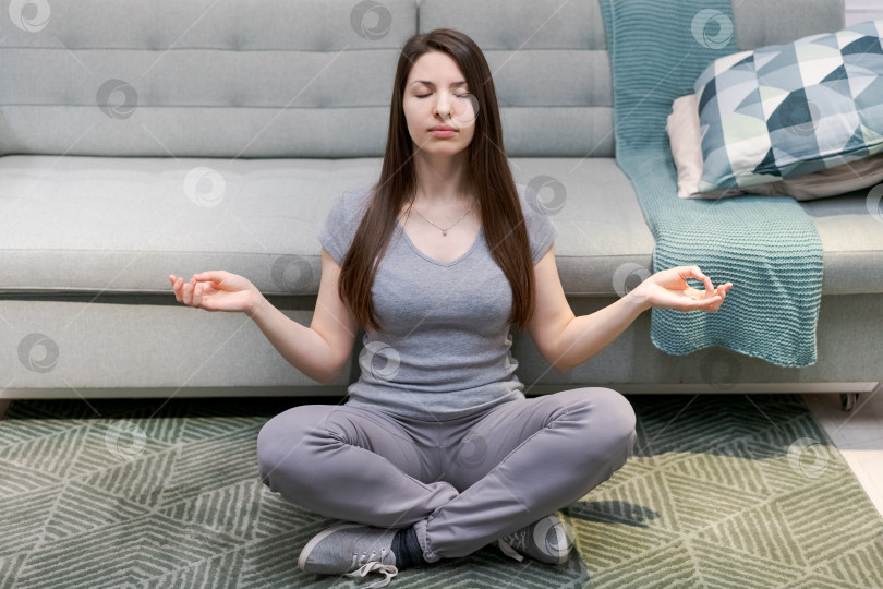 Скачать Женщина сидит на полу в гостиной и медитирует фотосток Ozero