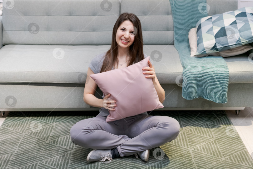Скачать На полу сидит женщина, держа в руках розовую подушку фотосток Ozero
