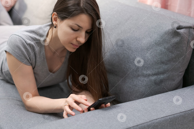 Скачать Женщина лежит на диване и смотрит в свой мобильный телефон фотосток Ozero