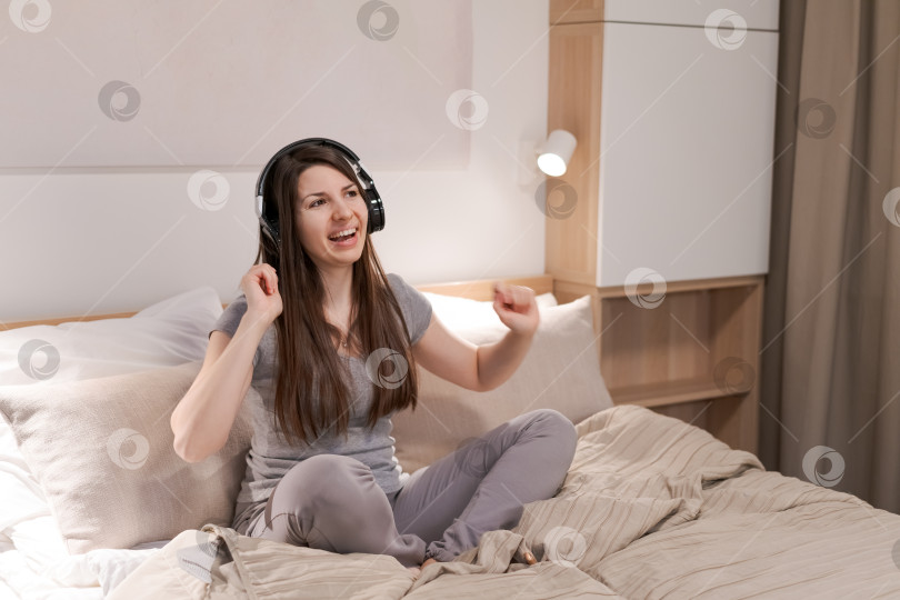 Скачать На кровати сидит женщина в наушниках фотосток Ozero