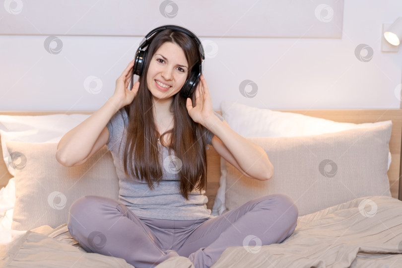 Скачать На кровати сидит женщина с наушниками на ушах фотосток Ozero