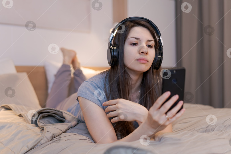 Скачать Женщина лежит на кровати с телефоном в руке фотосток Ozero