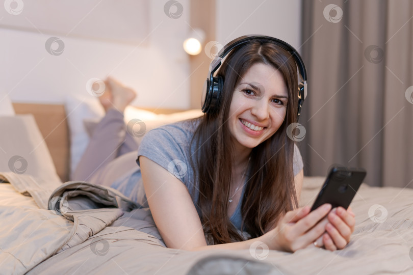 Скачать Женщина лежит на кровати с телефоном в руке фотосток Ozero