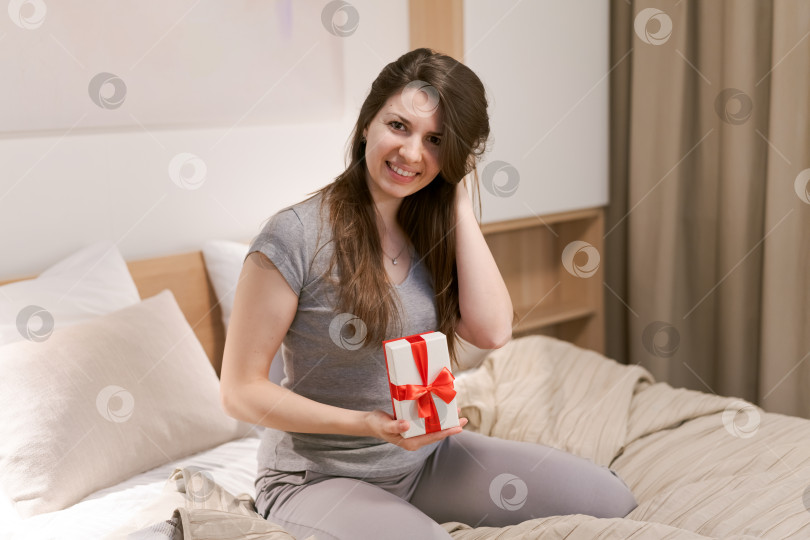 Скачать Женщина сидит на кровати, держа в руках красный подарок фотосток Ozero