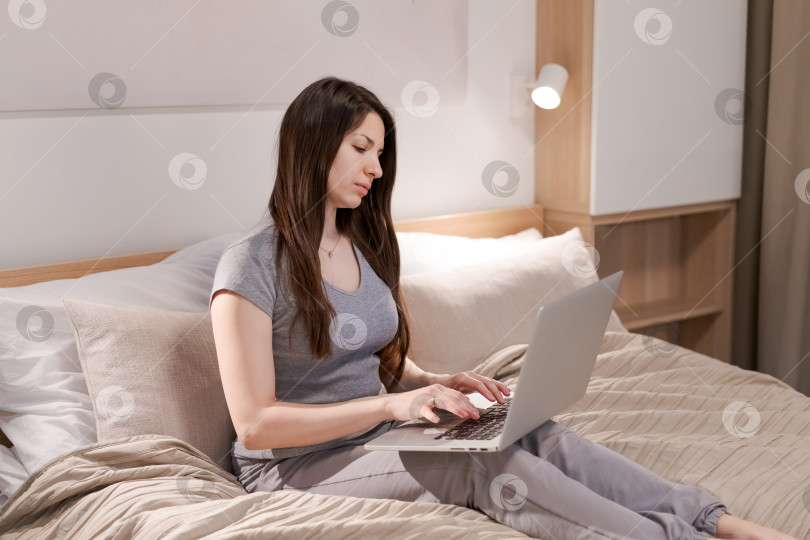Скачать На кровати сидит женщина, перед ней ноутбук фотосток Ozero