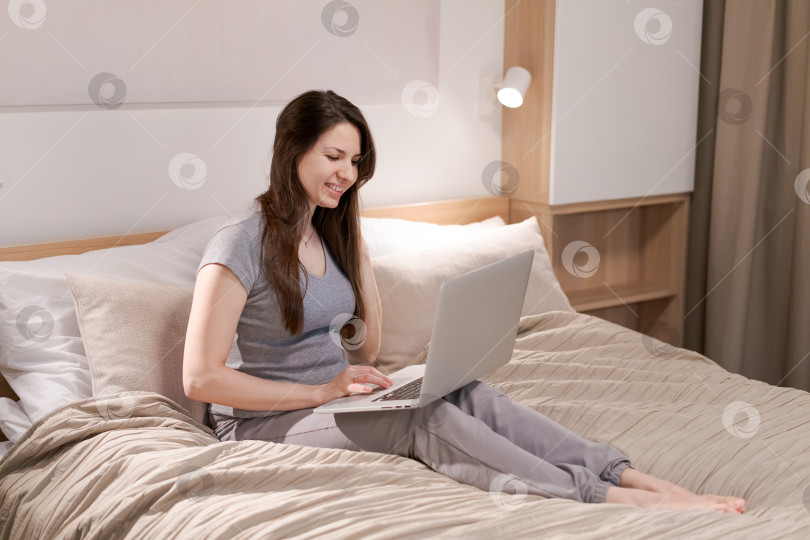 Скачать На кровати сидит женщина, перед ней ноутбук фотосток Ozero