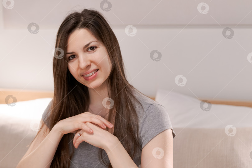 Скачать Женщина с длинными каштановыми волосами сидит на кровати и улыбается фотосток Ozero