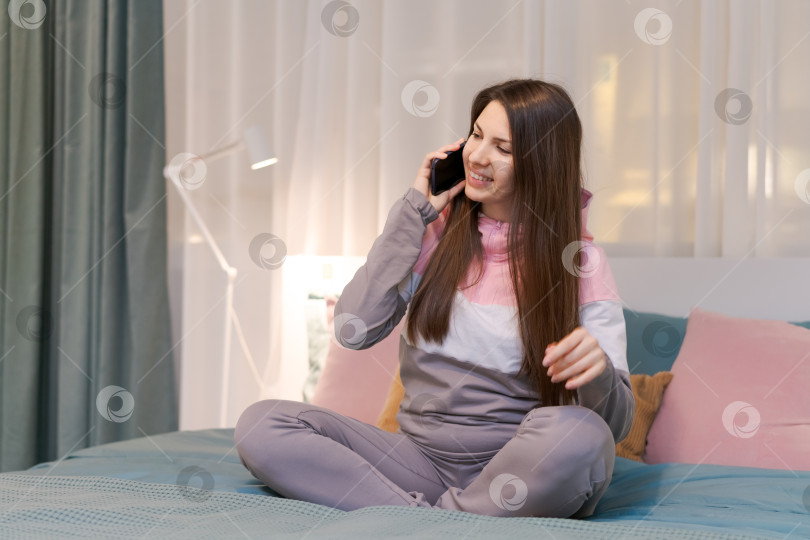 Скачать Женщина сидит на кровати и разговаривает по мобильному телефону фотосток Ozero