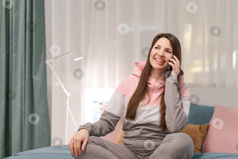 Скачать Женщина сидит на кровати и разговаривает по мобильному телефону фотосток Ozero
