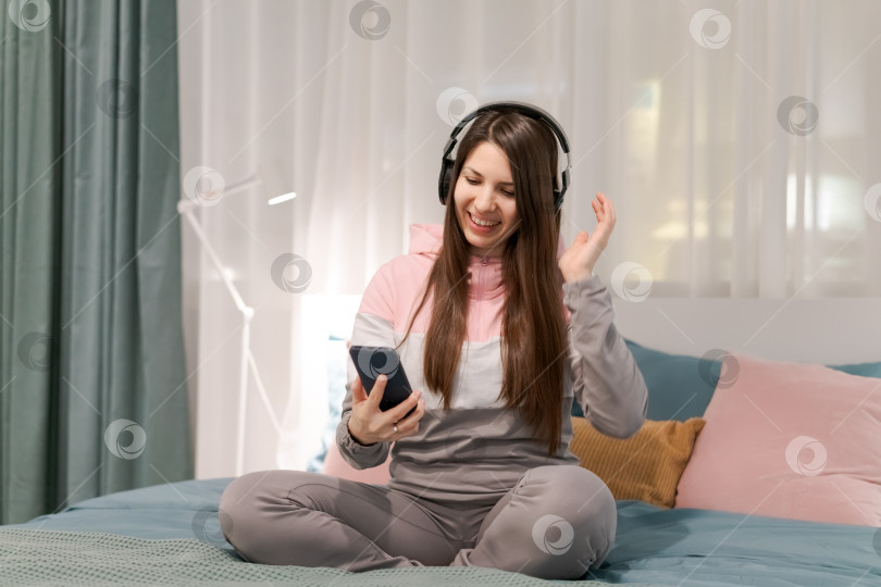 Скачать На кровати сидит женщина с сотовым телефоном в руке фотосток Ozero