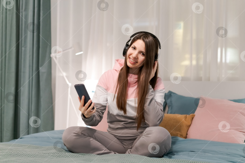 Скачать На кровати сидит женщина с мобильным телефоном в руке фотосток Ozero