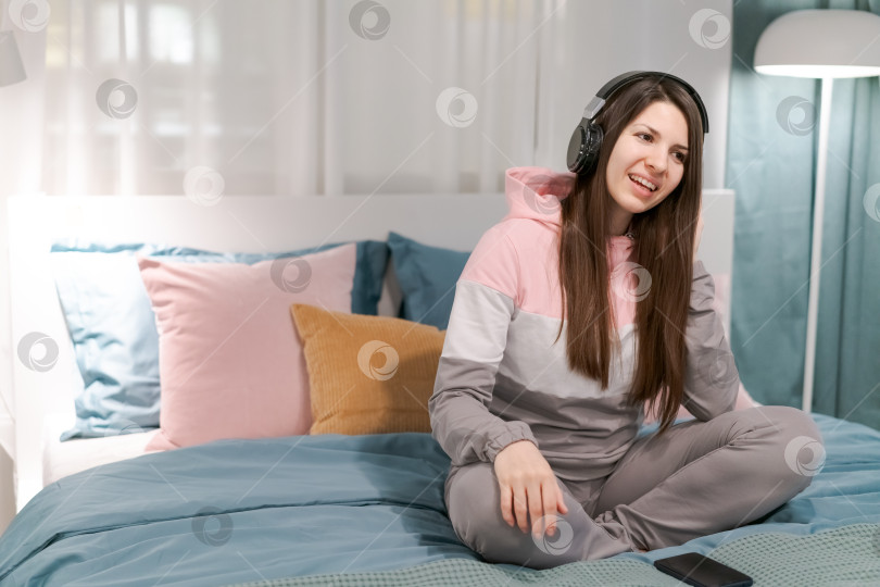 Скачать На кровати сидит женщина в наушниках фотосток Ozero