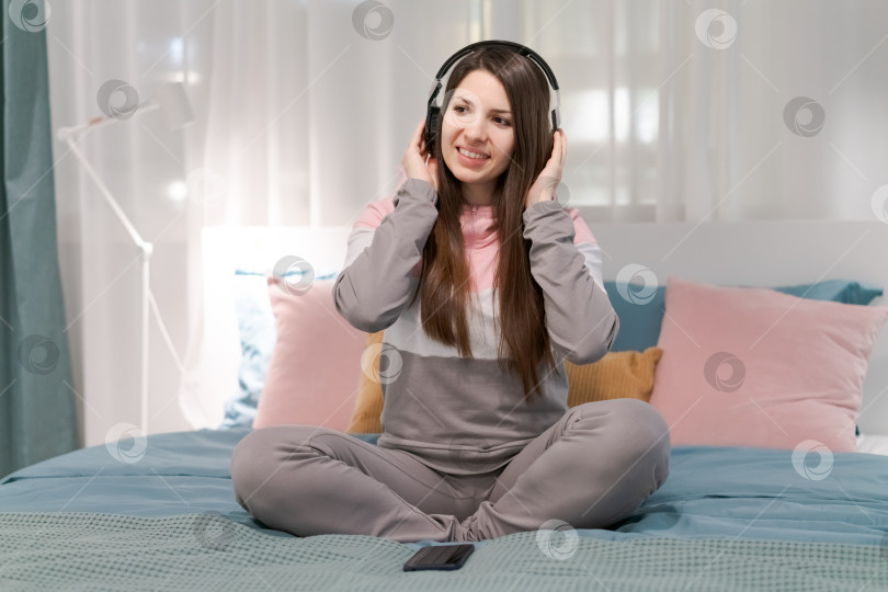 Скачать На кровати сидит женщина в наушниках фотосток Ozero