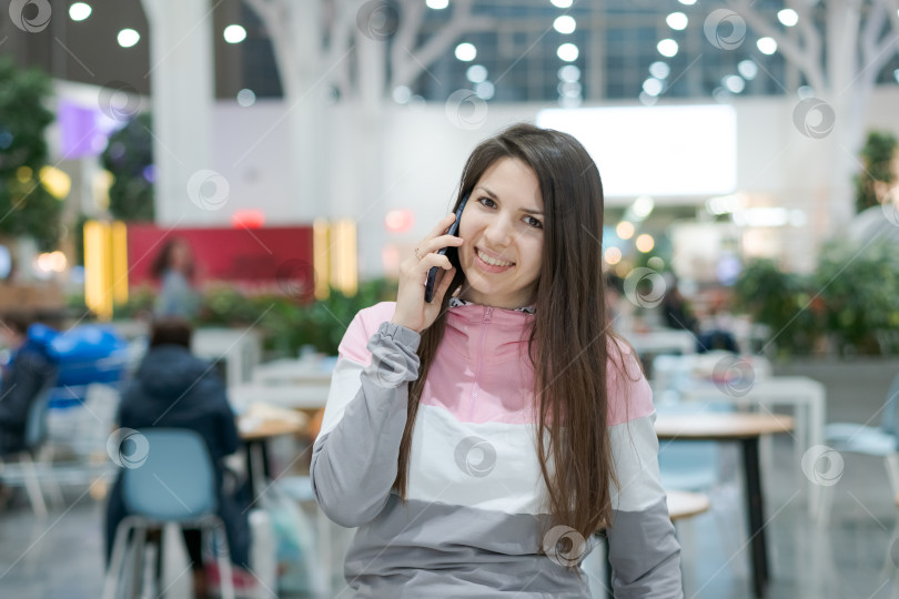 Скачать Женщина сидит за столиком в ресторане и разговаривает по мобильному телефону фотосток Ozero
