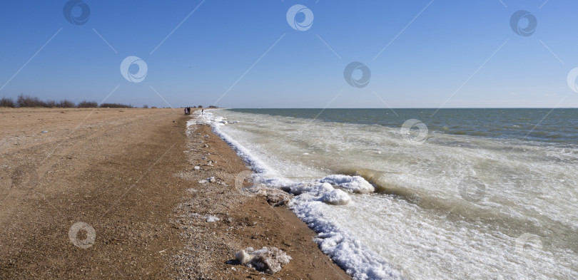 Скачать Зимний пляж на берегу моря с замерзшим песком, ледяными глыбами и снегом в воде. Снежно-ледяные дюны вдоль морского берега. Вдалеке люди прогуливаются вдоль береговой линии. Зимний морской пейзаж фотосток Ozero