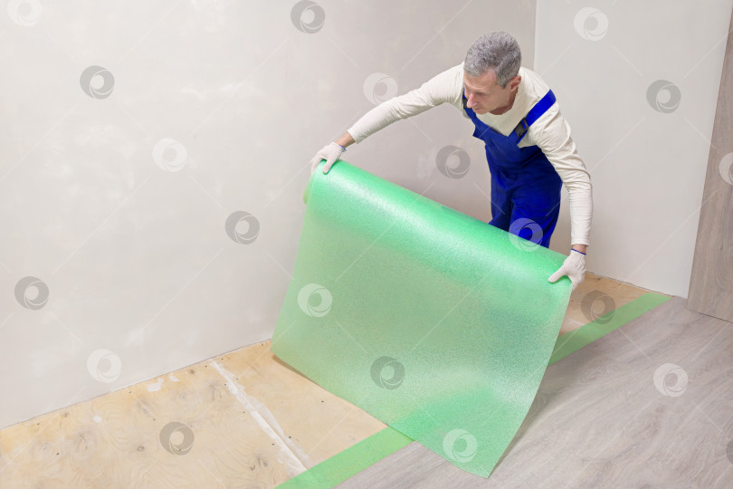 Скачать Мужчина в синем комбинезоне держит в руках кусок пластиковой пленки фотосток Ozero