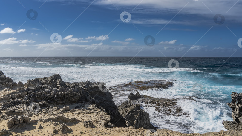 Скачать На побережье острова есть черные вулканические валуны. Волны бирюзового океана разбиваются о скалы, образуя белую пену. Облака на голубом небе. Маврикий. Остров Фуке фотосток Ozero