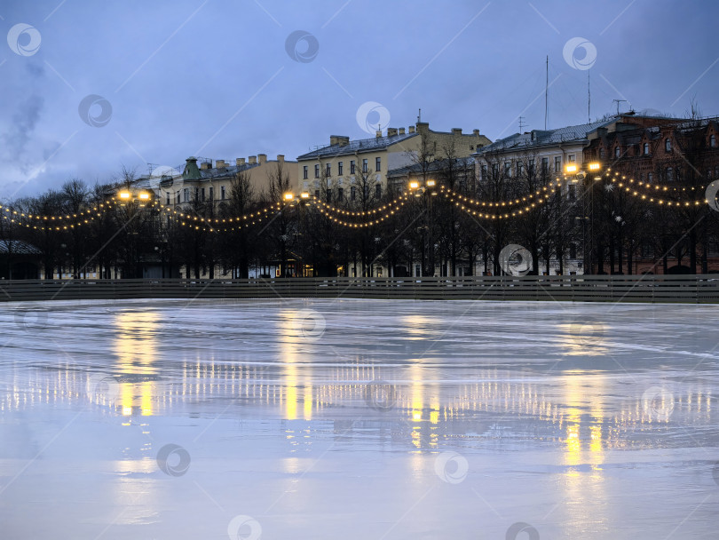 Скачать Санкт-Петербург, Россия - 17 декабря 2025 года. Вечерний вид ледового катка с отражениями и огнями. Снимок сделан на смартфон. фотосток Ozero