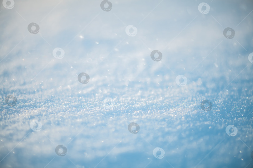Скачать Сверкающие снежные кристаллы создают текстурированную поверхность, отражающую солнечный свет и создающую абстрактный, холодный зимний фон с воздушным, нежно-голубым боке фотосток Ozero