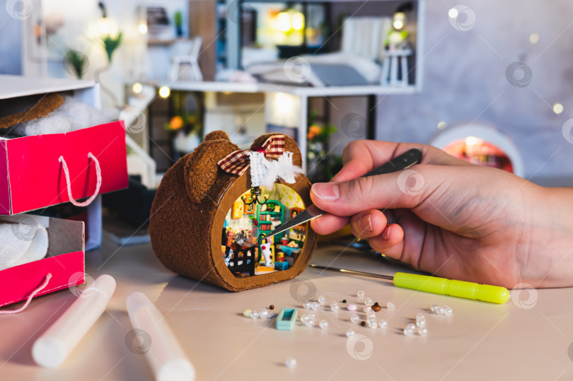 Скачать Девочка с помощью пинцета вешает зонтик на край кровати в крошечной комнатке фотосток Ozero