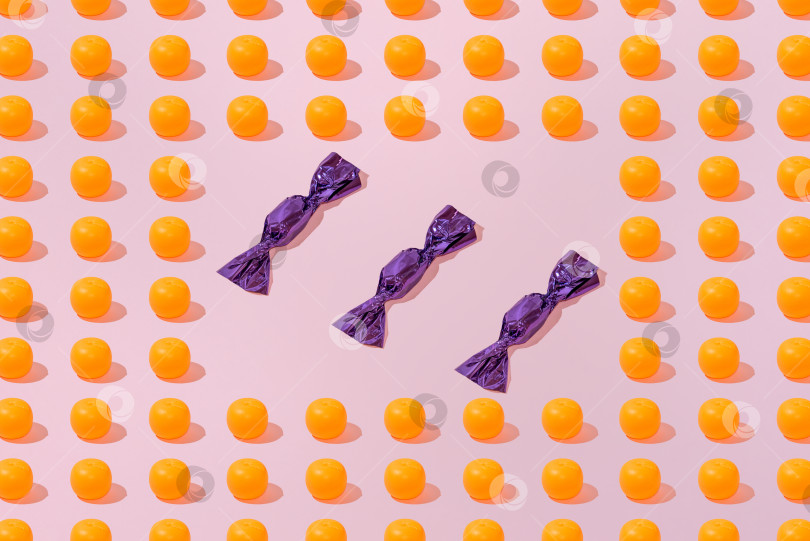 Скачать Креативный узор из апельсинов и конфет ровным слоем ложится на пастельно-розовый фон минимализм фотосток Ozero
