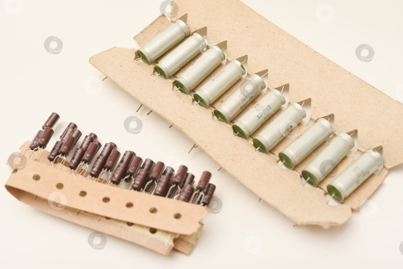 Скачать Старые конденсаторы в бумажной обертке. Алюминиевые конденсаторы на белом фоне. Электронные компоненты находятся в оригинальной упаковке. фотосток Ozero