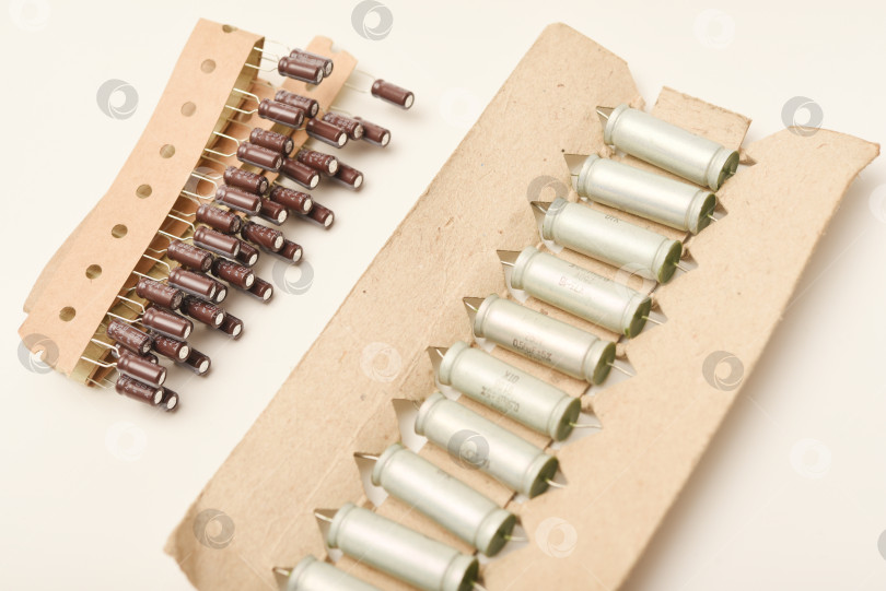 Скачать Старые конденсаторы в бумажной обертке. Алюминиевые конденсаторы на белом фоне. Электронные компоненты находятся в оригинальной упаковке. фотосток Ozero