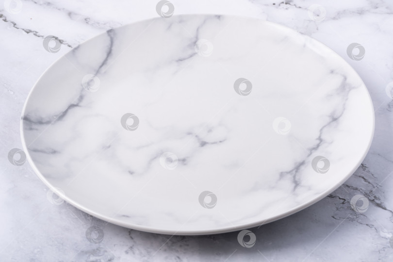 Скачать Круглая белая тарелка с мраморным рисунком на светлой поверхности для подачи блюд фотосток Ozero