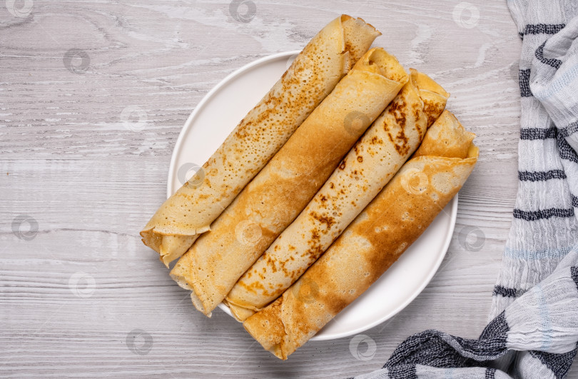 Скачать Мягкие и тонкие блинчики подаются на круглой белой тарелке на деревянном столе фотосток Ozero