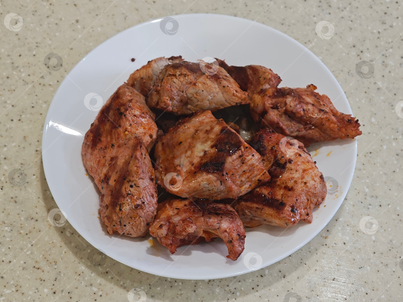 Скачать На белой тарелке кусочки мяса, приготовленные на электрическом гриле в помещении на кухне. На белой тарелке лежит мясо, приготовленное на электрическом гриле в закрытом помещении кухни. фотосток Ozero